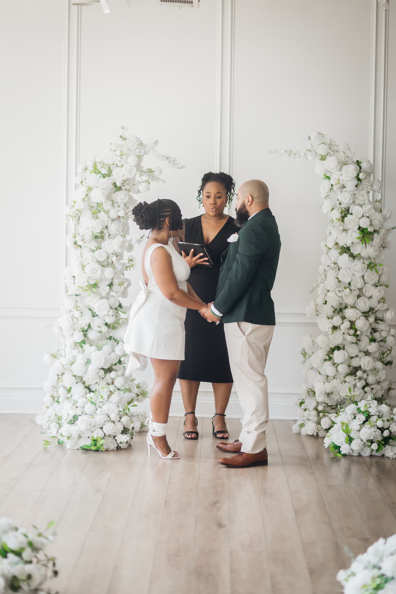 Jennifer Allen officiating a ceremony in front of white floral arches