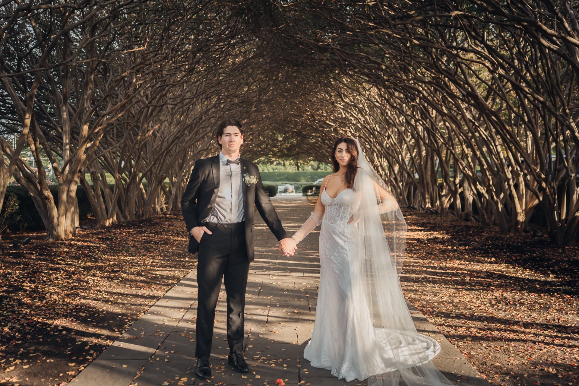 Just Elope couple standing hand in hand beneath an arch of bare trees